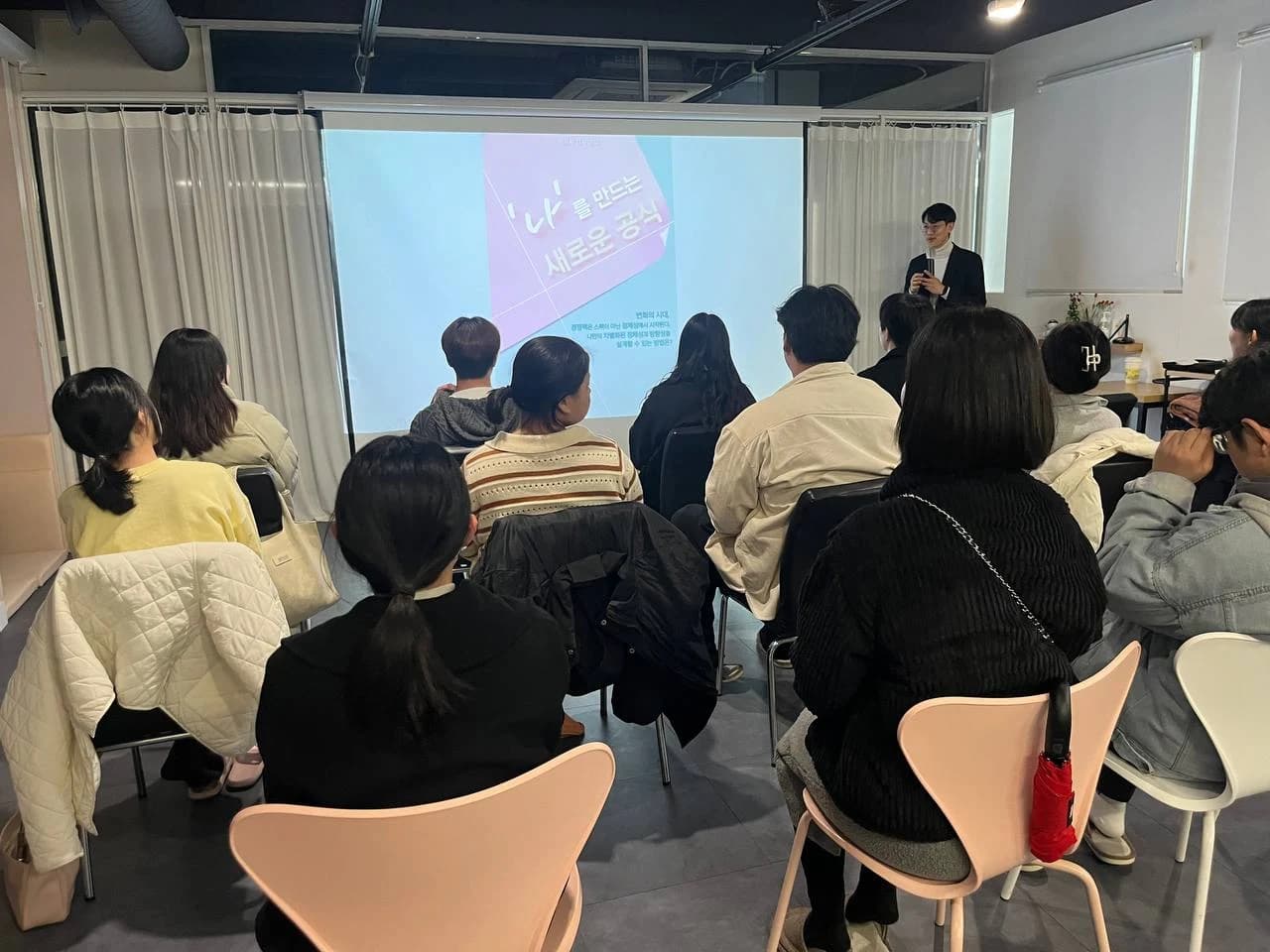스크린 앞에서 이야기를 전하는 발표자와 강의를 듣는 참여자들