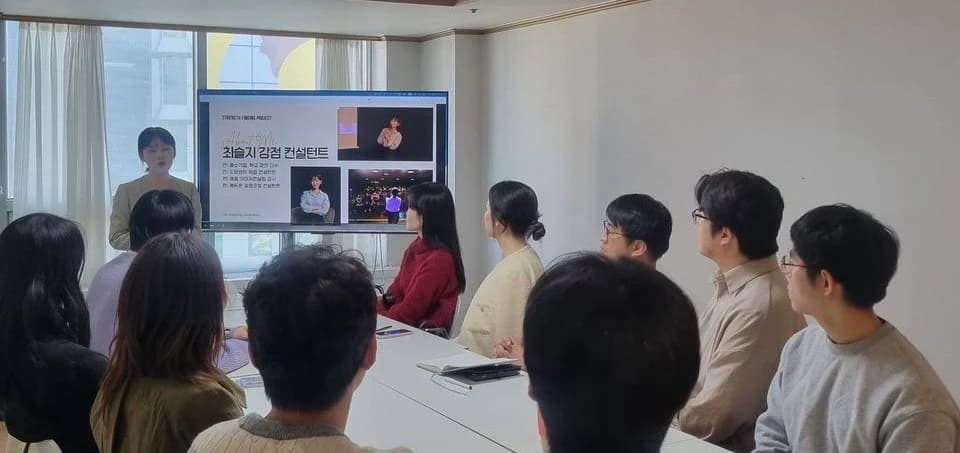테이블에 둘러앉아 화면을 보며 발표를 듣는 사람들